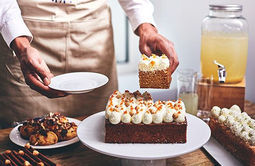 Accueil café et pauses sucrées -Maître d'hôtel servant une part de gâteau à un buffet sucré pour un accueil pause sucrée ou petit-déjeuner